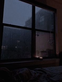 a bedroom with a window that has rain falling on the windows and lights shining in it