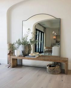 a mirror sitting on top of a wooden table next to a vase filled with plants