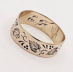 an antique gold wedding ring with flowers and leaves engraved on the side, set against a plain white background