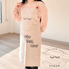 a woman standing in front of a mirror wearing an apron with eyelashes on it and the words live laugh love