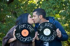 a man and woman kissing each other while holding up records with the words for the we are engaged written on them