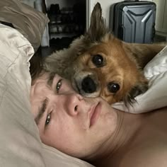 a woman laying in bed next to a dog on top of her head and looking at the camera