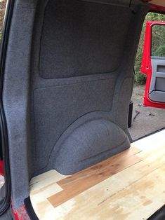 the back end of a red truck with its door open and wood planks on the floor