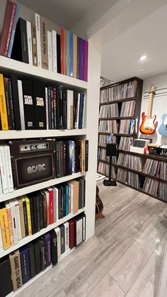 a book shelf filled with lots of books on top of a hard wood floor next to a guitar