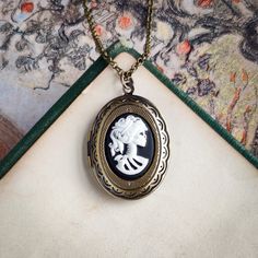 "Skeleton cameo on a vintage brass, antiqued, or shiny silver-plated oval locket, perfect for remembering your loved ones.  On 28 inches of chain. Choose your desired color.         I can change the chain to any length, just leave a note at checkout. Great for pictures of your loved ones.  Simply print, cut out, and attach a photo with glue.  We do not offer printer services at this time.  Fits a 17mm by 24mm oval photo. The box will include an oval stencil that will help you cut out your photo. Cameo Locket Necklace As Gift, Cameo Oval Pendant Locket Necklace Gift, Oval Cameo Locket Necklace Gift, Silver Oval Brass Locket Necklace, Oval Silver Brass Locket Necklace, Silver Oval Locket Necklace In Brass, Oval Silver Locket Necklace In Brass, Cameo Brass Oval Pendant Jewelry, Brass Cameo Oval Pendant Jewelry