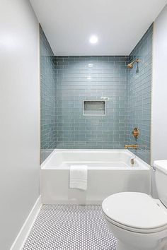 a white toilet sitting next to a bath tub under a bathroom window with blue tiles on the walls