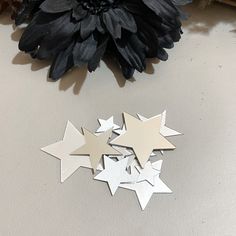 three metal stars next to a black flower on a white counter top with a dark flower in the background