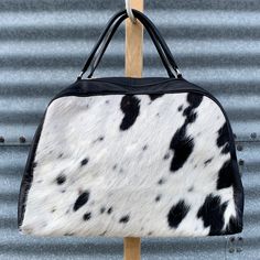 "Welcome to LuloTexas - all handmade, leather and cowhide purses, designed in Texas and hecho in Colombia. It's called, El Gordo - the Fat One in Spanish. It's the biggest, fattest weekend bag you'll ever own - all 100% cowhide chic. This beautiful bag is made of heavyweight but ultra soft black leather and a beautiful black and white hair-on hide on both sides. It's got one huge pocket on the side, and three smaller ones inside. It also has a leather attachable shoulder strap. Ain't nobody gonn White Leather Weekender Bag With Luggage Sleeve, White Leather Weekender Bag, Large Capacity White Leather Weekender Bag, White Leather Rectangular Weekender Bag, Black Bag With Cow Print For Everyday Use, Cowhide Duffle Bag, Leather Cow Print Bag For Everyday Use, Cowhide Makeup Bag, Cow Print Leather Bag For Daily Use