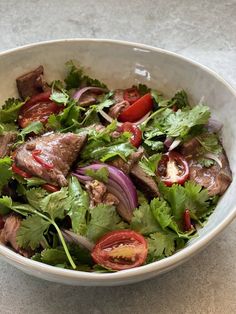 a white bowl filled with meat and vegetables on top of a marble counter next to a fork