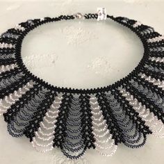 a black and white beaded necklace with silver beads on a white surface, in the shape of a fan