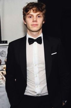 a young man in a tuxedo and bow tie standing next to a table