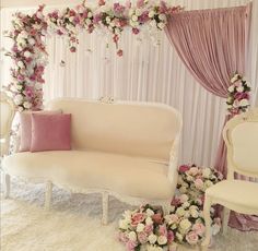 a white couch sitting under a pink and white flower covered arch next to a chair