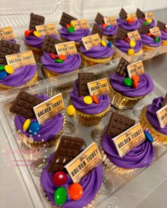 cupcakes decorated with candy and candies are on display in plastic trays