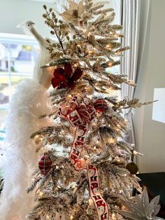 a white christmas tree decorated with red and gold ornaments, feathers and ribbons is in front of a window