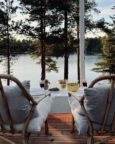 two chairs and a table on a deck overlooking the water with trees in the background