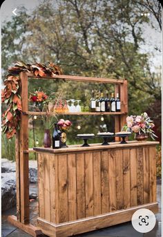 a wooden bar with bottles and flowers on it's top, next to a tree