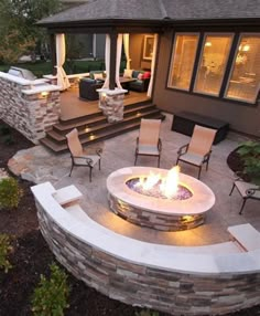 a fire pit in the middle of a patio with chairs around it and lights on