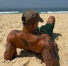 a man laying on top of a sandy beach next to the ocean with lots of tattoos