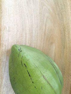 a green banana sitting on top of a wooden table