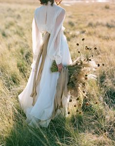 a woman in a white dress is walking through tall grass