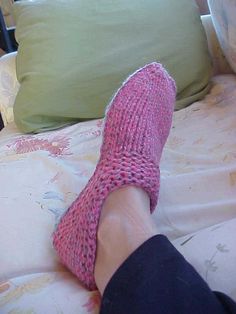 a person's feet in pink socks on top of a bed next to pillows