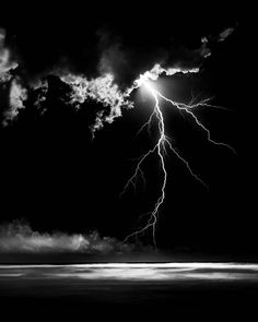 a black and white photo of a lightning bolt in the night sky over an ocean