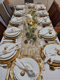 the table is set with white and gold plates, silverware, pine cones, and candlesticks