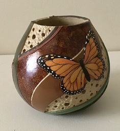 a small vase with a butterfly painted on the side and holes in the bottom, sitting on a white surface