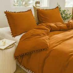 an orange comforter with pom - poms on the edges sits in front of a window