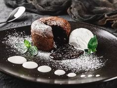 a chocolate dessert on a black plate with powdered sugar and mint sprinkles