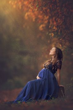 a pregnant woman sitting in the grass with her eyes closed, looking up into the sky