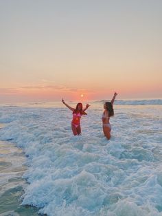 two women in bikinis are playing in the water at sunset on the ocean shore