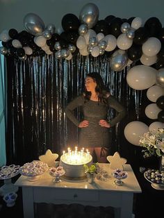 a woman standing in front of a cake with candles on it and balloons behind her