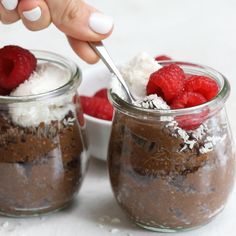 two jars filled with chocolate pudding and topped with raspberries, whipped cream and powdered sugar