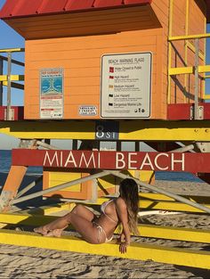 a woman sitting on top of a yellow lifeguard tower next to the ocean in miami beach