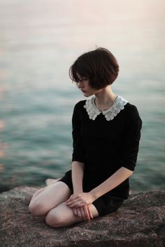 a woman sitting on top of a rock near the water