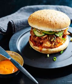 a sandwich with cucumbers and sauce on a black plate next to a spoon