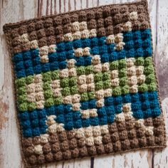 a crocheted square is sitting on a wooden surface, with the pattern in blue and green