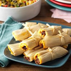 several tamales on a blue plate next to a bowl of salad