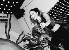 a black and white photo of a woman on a bike in a room with lights