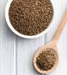 a wooden spoon filled with brown seeds on top of a white wood table next to a bowl