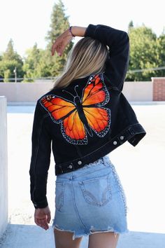 a woman wearing a jacket with a butterfly painted on it's back, standing next to a wall