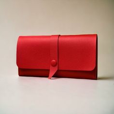 a red leather purse with a ribbon on the front and side, sitting on a white surface