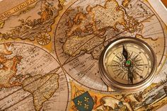 a compass is sitting on top of an old world map with other maps in the background