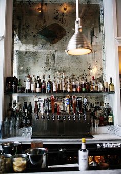 a bar with lots of liquor bottles and glasses on it's shelves, next to a light fixture