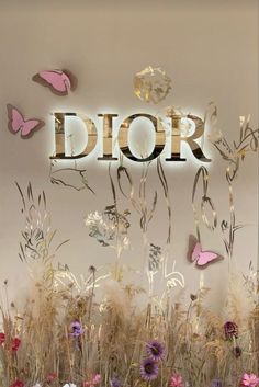 the word dior surrounded by flowers and butterflies in front of a white wall with gold lettering