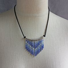 "Adjustable seed bead bib necklace in varied hues of blue, is made of a beaded fringe pendant with blue seed beads that dangle from a silver plated brass tube with silver steel beads. The beaded fringe is put on black round cotton cord with a sliding knot to adjust the necklace from a choker to a long pendant. ❖ glass seed beads ❖ silver plated brass tube ❖ steel beads ❖ cotton cord Necklace adjusts from 13 - 24\" in length." Adjustable Blue Beaded Necklace With Dangling Beads, Adjustable Blue Beaded Strand Necklace, Blue Adjustable Beaded Necklace, Blue Beaded Fringe Jewelry For Gifts, Cheap Blue Beaded Fringe Jewelry, Blue Beaded Fringe Necklace For Festival, Sliding Knot Necklace, Dark Blue Seed Bead Necklace, Blue Round Beads With Beaded Fringe