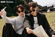 two young men sitting on the ground with their arms around each other and reading papers