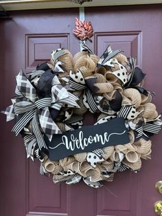 a welcome wreath hanging on the front door with black and white ribbon around it that says welcome