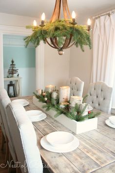 a dining room table with candles on it and christmas decorations hanging from the chandelier